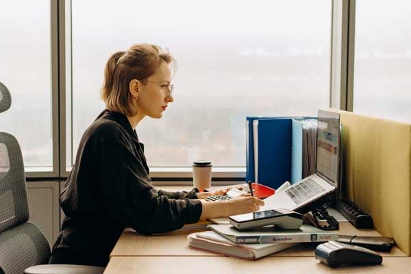 Woman working at computer with books and large window near